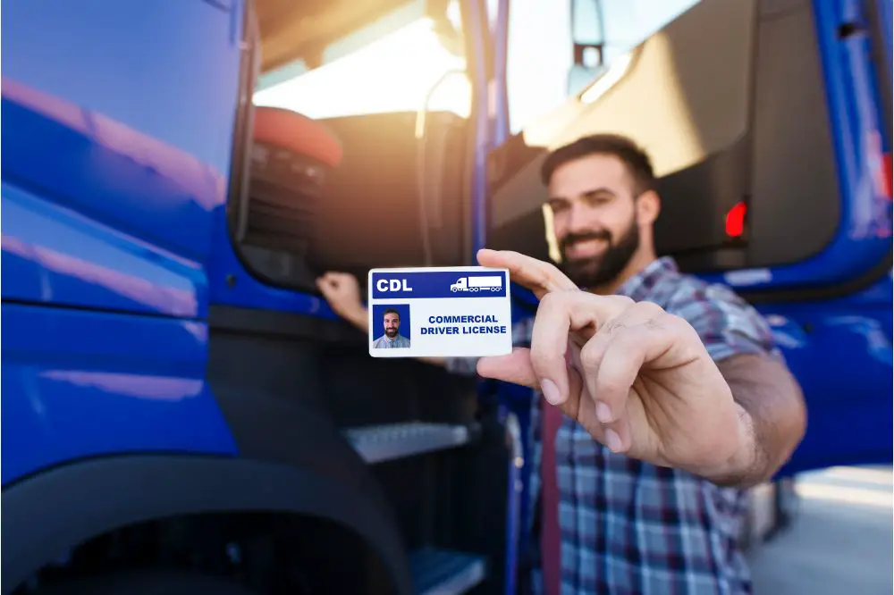 truck driver standing by his truck and showing his commercial driver license