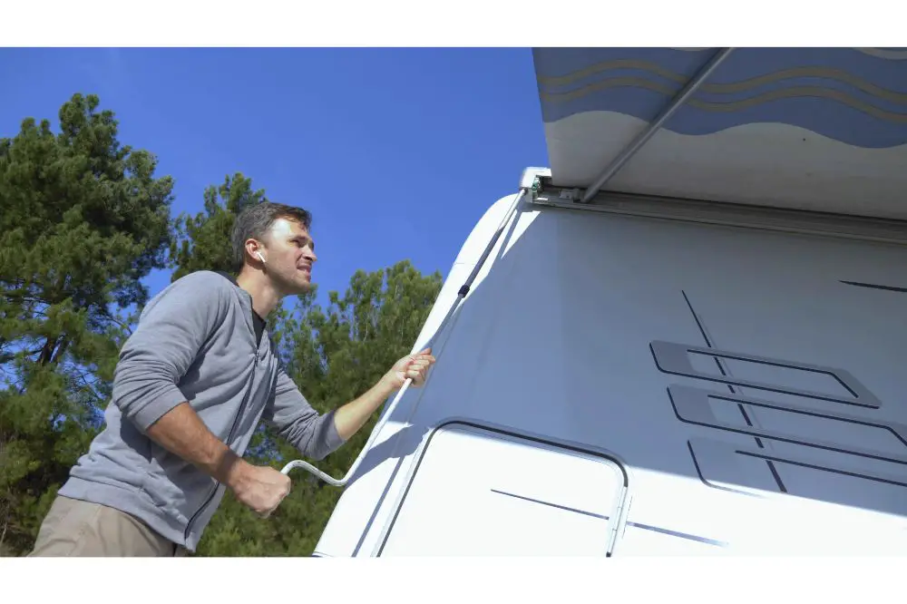 A man sets up a canopy from the sun on a motor home against a clear blue sky